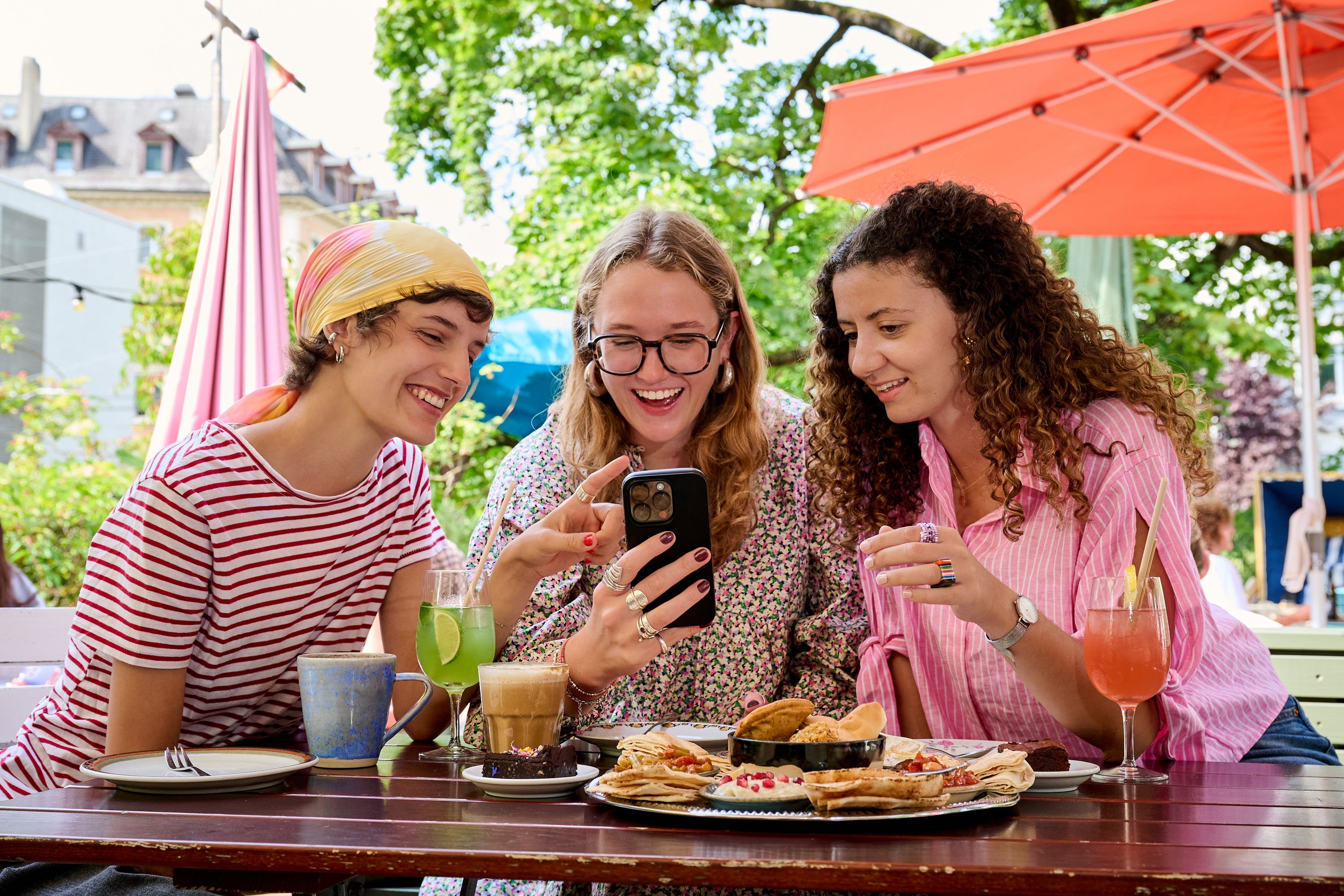 Three friends enjoying outdoor brunch in Kleine Freiheit cafe, wearing mesme wrap nails looking at a phone together.