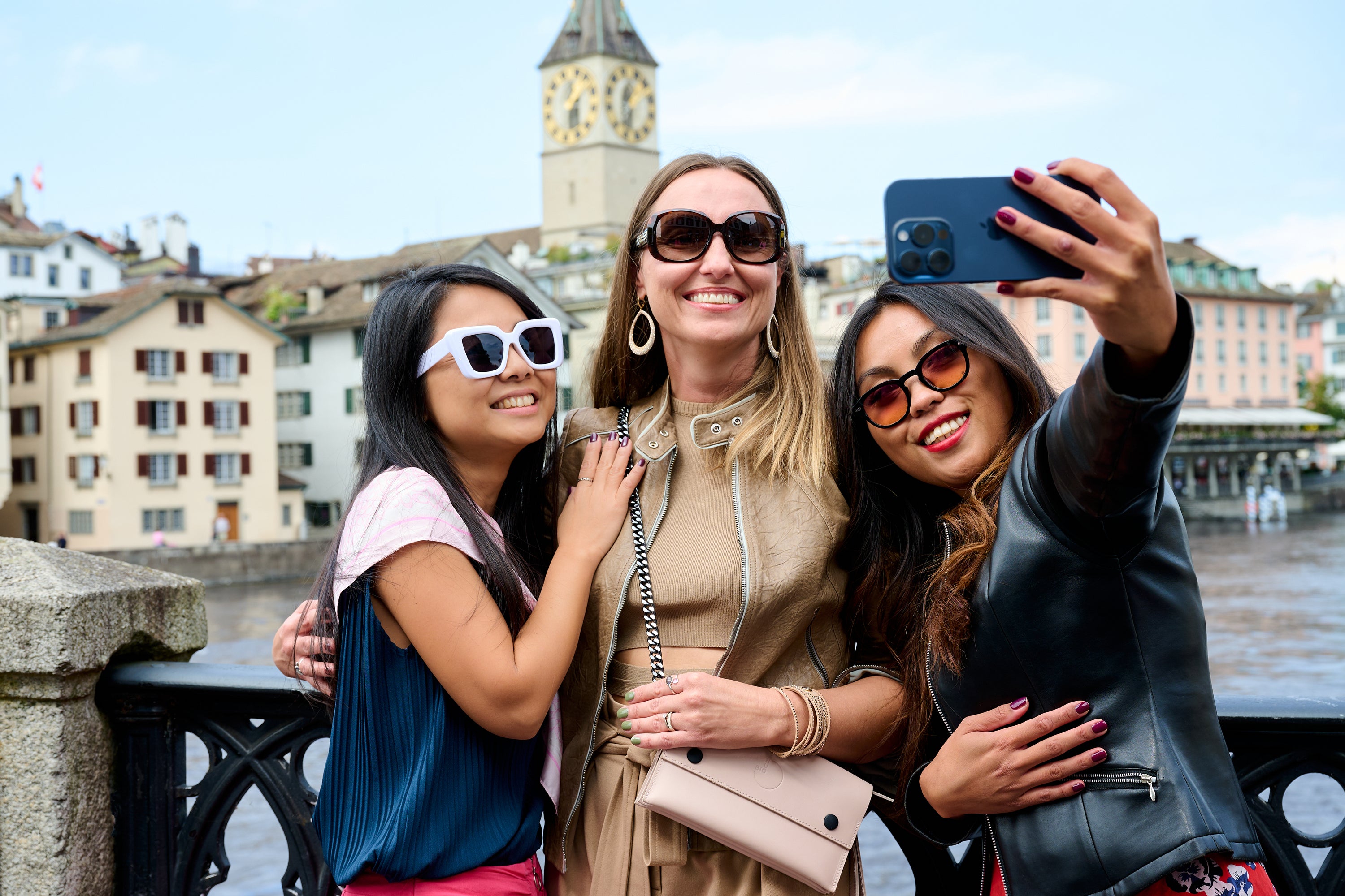 Three women taking a selfie with a scenic Zurich background on Münsterbrücke